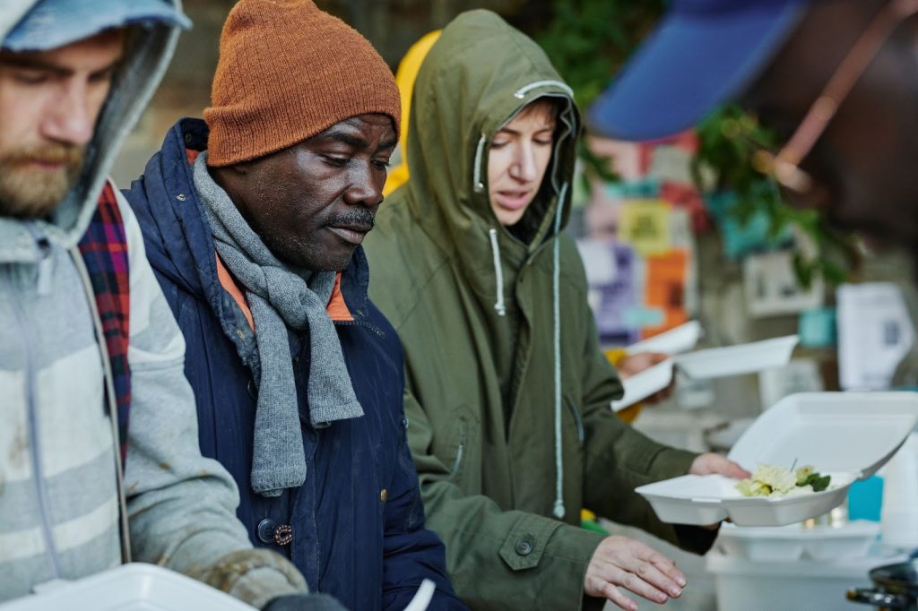Alt title: Homeless men getting a meal
Alt text: Three men in coats eating a meal.