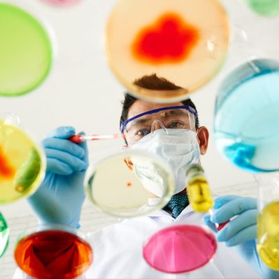 A man in a white lab coat with substances in clear dishes