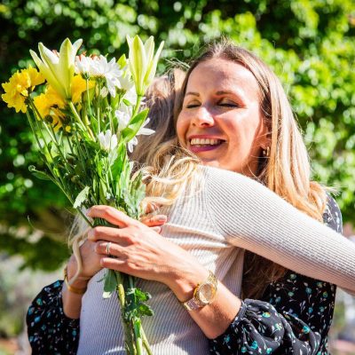 Two people hugging, one holding flowers